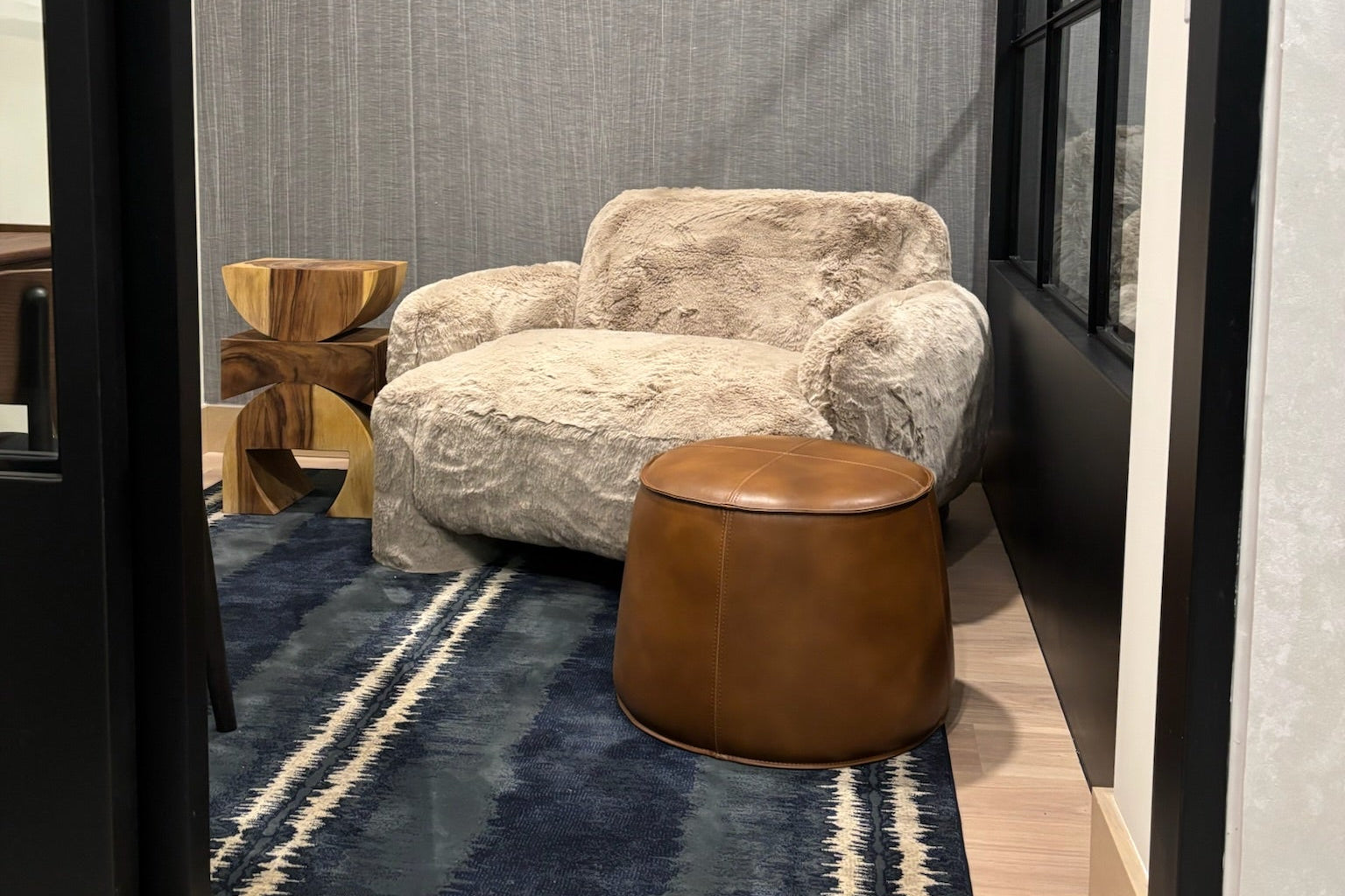 Modern interior with a textured wall, wooden chair, and round table on a blue rug.