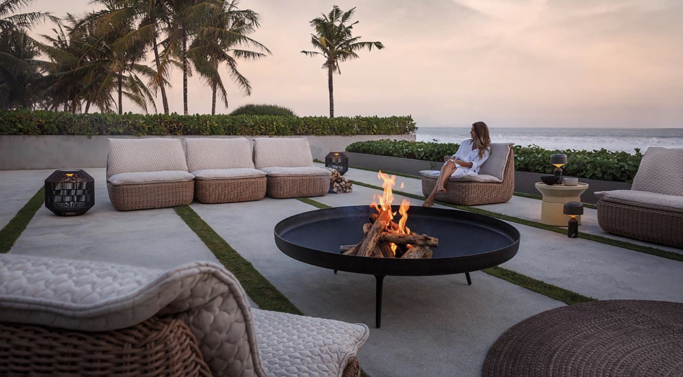 Woman sitting by a firebowl on a patio with ocean view